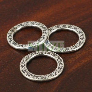 May include: Three silver-colored metal rings with a floral pattern. The rings are arranged in a cluster on a dark brown surface. The rings have a textured appearance and a circular shape.