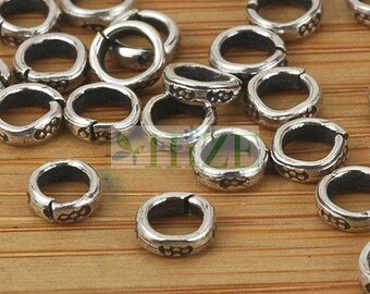 May include: A close-up of a group of silver jump rings with a decorative design. The rings are arranged in a random pattern on a wooden surface.