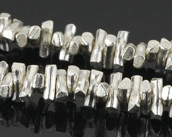 May include: A close-up of a silver chain made of small, irregular, textured, and elongated beads.