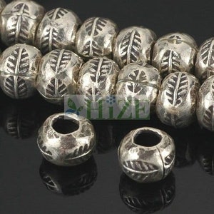 May include: A strand of silver beads with a leaf design. The beads are round and have a hole in the center. There are two loose beads in the foreground.