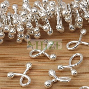 以下が含まれることがあります： ねじれたデザインと丸みを帯びた端を持つ銀色の金属製の留め具。留め具は木製の表面に配置されています。