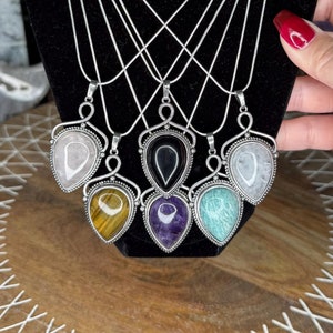 May include: Seven silver necklaces with teardrop-shaped pendants featuring various gemstones. The gemstones include clear, black, white, yellow, purple, and green.