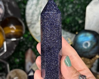 May include: A dark blue, sparkly, pointed crystal tower. The crystal is smooth and has a polished finish.