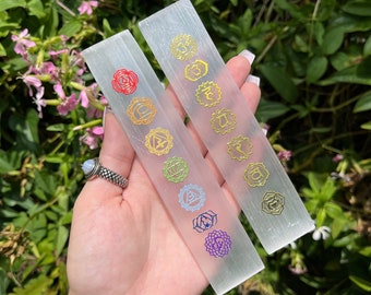 May include: Two white selenite wands with gold chakra symbols. The symbols are in the colors of the seven chakras: red, orange, yellow, green, blue, indigo, and violet.