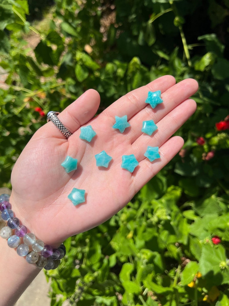 May include: A collection of eight teal green star-shaped stones, also known as star-shaped crystals, are displayed on a hand. The stones are smooth and polished.