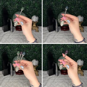 May include: Silver-toned spoons with decorative handles and gemstone accents. Each spoon has a different coloured gemstone, including green, purple, and blue. The spoons have ornate, detailed bowls. The spoons are displayed against a backdrop of green foliage.