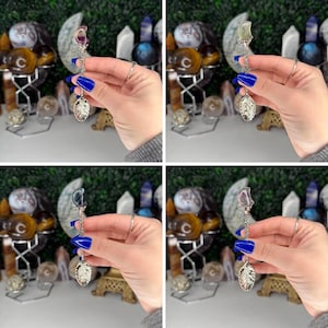 May include: A silver spoon with a decorative handle and a gemstone at the top. The spoon has a leaf-shaped bowl. The gemstones are various colours, including purple, clear, and blue. The background includes other decorative items.