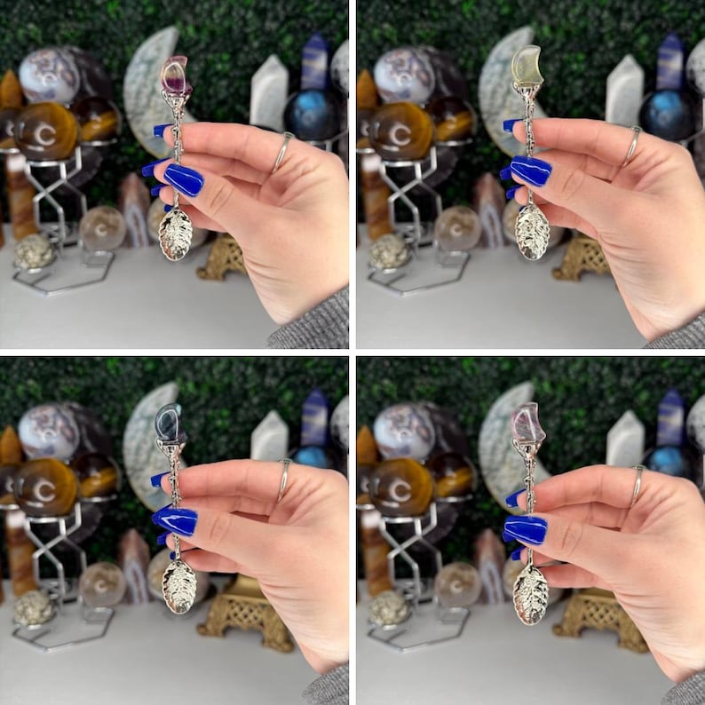 May include: A silver spoon with a decorative handle and a gemstone at the top. The spoon has a leaf-shaped bowl. The gemstones are various colours, including purple, clear, and blue. The background includes other decorative items.