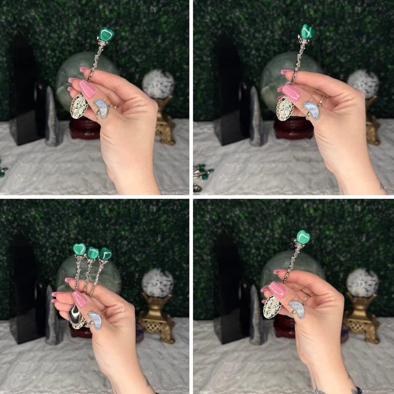 May include: Silver decorative spoons with green gemstone details. The spoons have ornate handles and a decorative bowl. The gemstones are heart-shaped or round. The spoons are held in a hand against a backdrop of crystals and greenery.