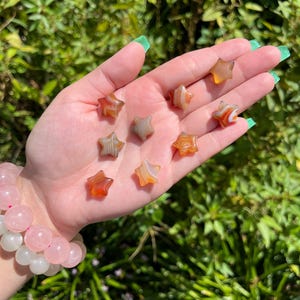 May include: A collection of eight agate star-shaped stones in shades of brown, orange, and white. The stones are arranged on a hand.