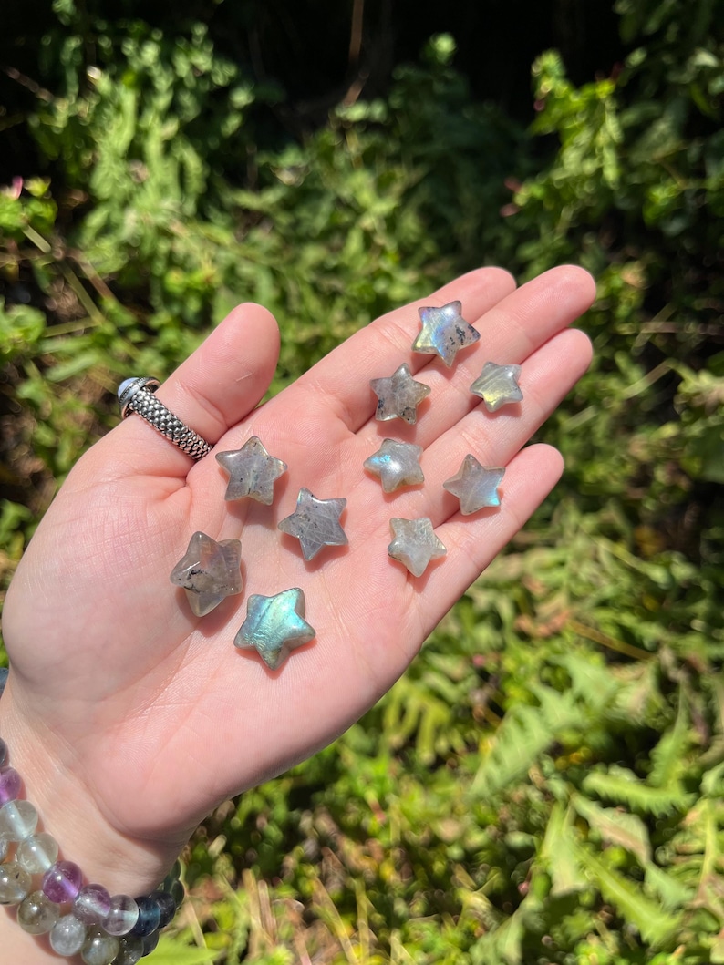 May include: A collection of nine iridescent labradorite star-shaped crystals. The crystals are a light grey color with blue and green iridescent flashes.