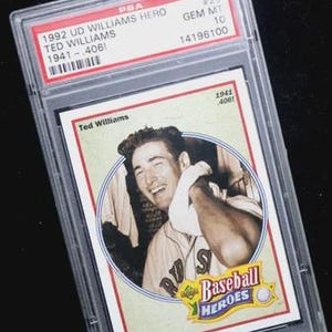 May include: A 1992 UD Williams Hero baseball card, graded by PSA. The card features a portrait of Ted Williams and the text "Baseball Heroes". The card is encased in a clear protective holder with the PSA grading information visible.
