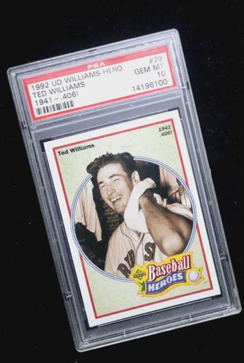May include: A 1992 UD Williams Hero baseball card, graded by PSA. The card features a portrait of Ted Williams and the text "Baseball Heroes". The card is encased in a clear protective holder with the PSA grading information visible.