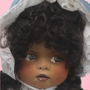 May include: A vintage doll with dark curly hair, blue eyes, and rosy cheeks. The doll wears a white dress and a blue bonnet with lace trim. The doll's face has a serene expression.