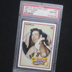 May include: A 1992 Upper Deck Ted Williams baseball card, encased in a protective holder. The card features a portrait of Ted Williams and the text "Baseball Heroes". The holder has a PSA label with details.