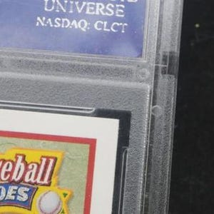 May include: A close-up of a baseball card encased in a clear plastic holder. The card features the words "Baseball Heroes" in a yellow and red design. The top of the holder has a blue label with white text, including "UNIVERSE" and "NASDAQ: CLCT".