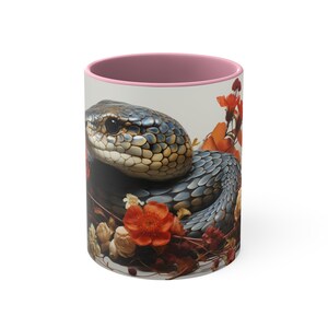 Peut inclure: Une tasse en céramique rose avec un intérieur blanc et une image colorée d'un serpent enroulé autour de fleurs. Le serpent est bleu, noir et jaune, et les fleurs sont rouges, orange et blanches.
