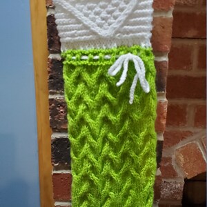 May include: A green and white knitted Christmas stocking with a cable knit pattern. The stocking has a white cuff and a white bow at the top.