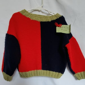 Könnte beinhalten: Ein handgestrickter Pullover mit roten, blauen und grünen Streifen. Der Pullover hat einen Rundhalsausschnitt und lange Ärmel. Das Etikett lautet "Handmade by Karen Flecchia".