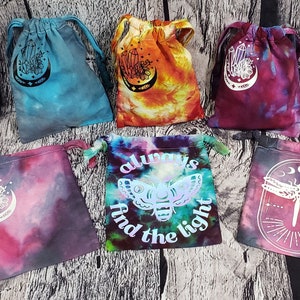 May include: Six tie-dye drawstring bags with various designs. The designs include crystals, a moth with the text "always find the light", and a dragonfly.