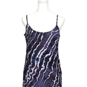 May include: A sleeveless tank top with thin straps, featuring a tie-dye pattern of dark blue and white wavy stripes. The top is displayed on a white mannequin, showcasing its design and fit. The fabric appears soft and lightweight.