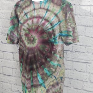 May include: A short-sleeved tie-dye t-shirt in shades of purple, green, and blue. The shirt features a spiral pattern radiating from the center. The t-shirt is displayed on a white mannequin.