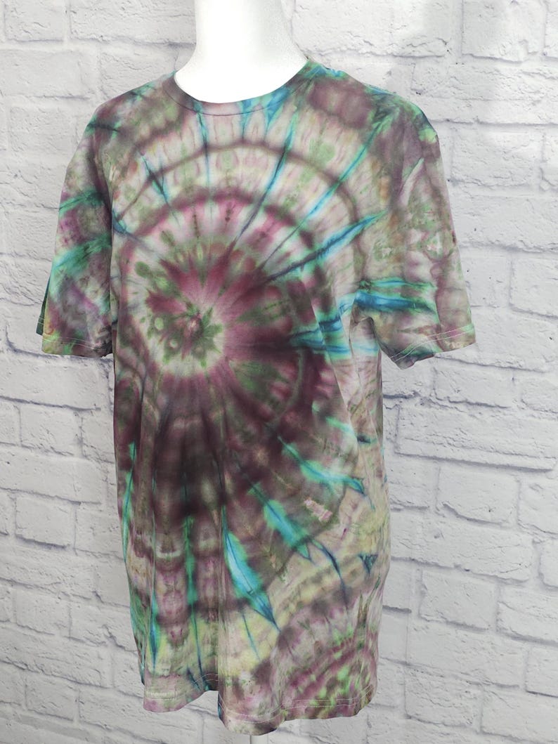 May include: A short-sleeved tie-dye t-shirt in shades of purple, green, and blue. The shirt features a spiral pattern radiating from the center. The t-shirt is displayed on a white mannequin.