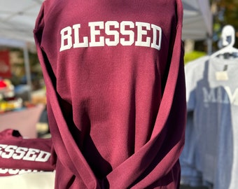 May include: A maroon sweatshirt with the word "BLESSED" printed in white on the front.