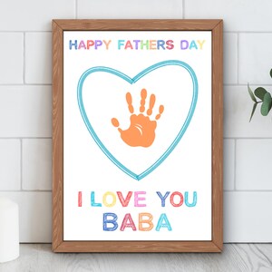 May include: A framed print with a white background features the text "HAPPY FATHERS DAY" and "I LOVE YOU BABA" in colourful letters. A blue heart shape surrounds an orange handprint. The frame is made of brown wood.