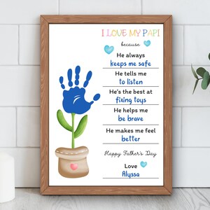 May include: A framed print with the text "I LOVE MY PAPI" and a blue handprint flower design. The print includes phrases like "He always keeps me safe" and "Happy Father's Day." The print is in a brown wooden frame.