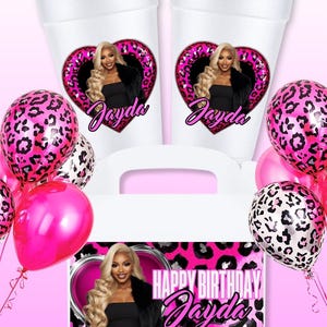 K&ouml;nnte beinhalten: Ein Party-Set mit wei&szlig;en Bechern und einer Geschenkbox, verziert mit einem rosa Leopardenmuster und einem Foto einer Frau. Die Becher und die Box tragen den Namen "Jayda" und den Schriftzug "Happy Birthday Jayda". Rosa Ballons erg&auml;nzen das Set.