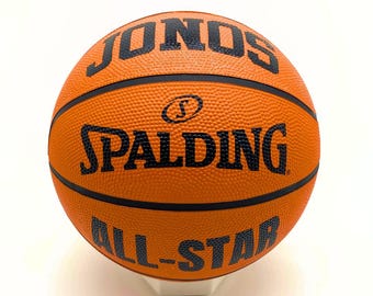 May include: An orange basketball with black markings. The Spalding logo and "All-Star" are printed on the ball. The word "JONS" is printed on the top of the ball.