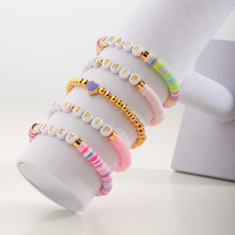 May include: Five colourful beaded bracelets with white letter beads spelling out the names "GRACE", "ISTRIP", "ISTRIP", "RILEY", and a purple heart charm.