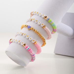 May include: Five colorful beaded bracelets with white letter beads spelling out the names "GRACE", "ISTRIP", "ISTRIP", "RILEY", and a purple heart charm.