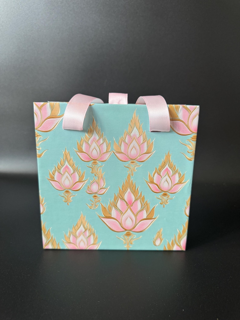 May include: A light blue gift bag with pink and gold lotus flower designs and pink ribbon handles.