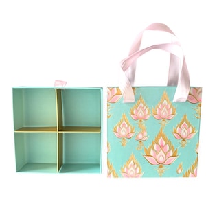 May include: A two-piece gift set featuring a teal box with four compartments and a matching tote bag. The tote bag has pink handles and a teal background with a repeating pattern of pink and gold lotus flowers.