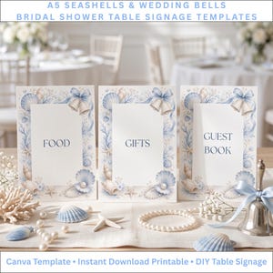 May include: Three A5 vertical rectangular signs with white backgrounds and blue borders featuring illustrations of seashells, wedding bells, pearls, and coral. The signs display the text FOOD, GIFTS, and GUEST BOOK in dark blue font.