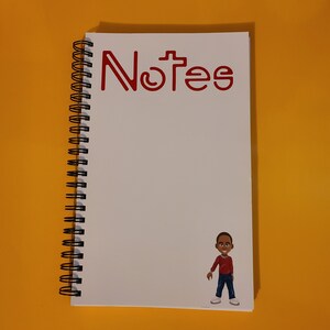 Può includere: Un quaderno a spirale bianco con la parola "Notes" in lettere rosse sulla copertina. Un'illustrazione di un cartone animato di una persona giovane si trova nell'angolo in basso a destra della copertina.