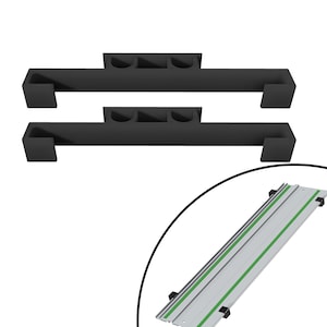 Puede incluir: Dos soportes de metal negro con tres ranuras cada uno, diseñados para sujetar un sistema de rieles. El sistema de rieles es un riel de metal plateado con líneas verdes que lo recorren.