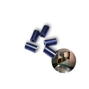 Op de afbeelding: Zes donkerblauwe rubberen doppen voor een printer of ander apparaat. De doppen zijn cilindrisch met een klein gaatje in het midden. Een close-up van een metalen onderdeel van een printer met een messing buis is ook te zien.