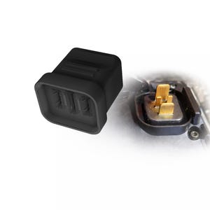 Op de afbeelding: Een zwarte rechthoekige behuizing voor een elektrische connector met een getextureerd buitenoppervlak en een holle binnenkant. Daarnaast is een bijpassend onderdeel geïnstalleerd, met vier goudkleurige metalen pinnen op een vierkante basis.