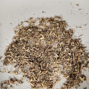 May include: A white ceramic bowl filled with a mixture of dried herbs and white salt.