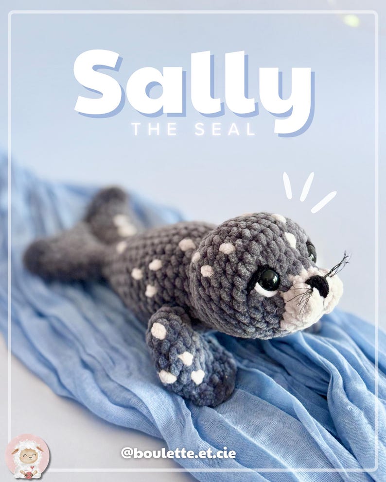K&ouml;nnte beinhalten: Ein handgefertigtes geh&auml;keltes Seehund-Pl&uuml;schtier in Grau und Wei&szlig; mit dem Text "Sally the Seal". Der Seehund hat wei&szlig;e Flecken, schwarze Augen und eine wei&szlig;e Schnauze. Er liegt auf blauem Stoff.