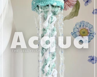 May include: A handmade crocheted jellyfish in blue and white, with trailing tentacles. The jellyfish is hanging from a wooden rod. The word "Acqua" is displayed in large white letters, with "THE JELLYFISH" below.