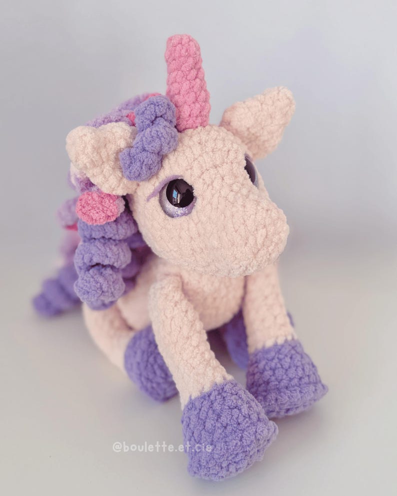 Pode incluir: Um unic&oacute;rnio de pel&uacute;cia feito &agrave; m&atilde;o em cores pastel suaves. O unic&oacute;rnio apresenta um corpo rosa, cascos e crina roxos e um chifre rosa. Olhos grandes e reflexivos d&atilde;o ao brinquedo uma apar&ecirc;ncia caprichosa. O brinquedo &eacute; feito de um material texturizado e difuso.