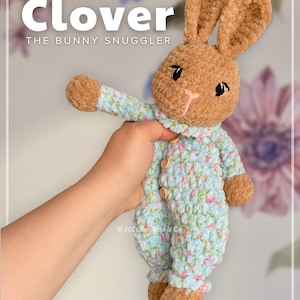 May include: A handmade brown bunny plush toy wearing a light blue floral print onesie. The text "Clover THE BUNNY SNUGGLER" is at the top. The plush is held by a hand. The bottom of the image has the text "@boulette.et.cie".