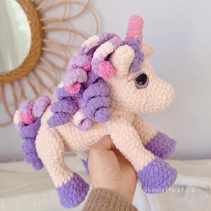 Pode incluir: Um brinquedo de unic&oacute;rnio de pel&uacute;cia feito &agrave; m&atilde;o em cores pastel suaves. O unic&oacute;rnio tem um chifre rosa, uma crina roxa e rosa e cascos roxos. O corpo &eacute; rosa claro. O brinquedo &eacute; segurado em uma m&atilde;o.