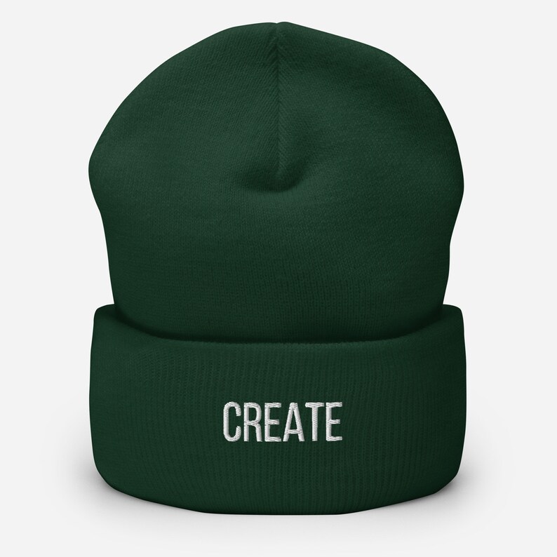 Puede incluir: Un gorro de lana verde oscuro con la palabra "CREATE" bordada en blanco en la parte delantera.
