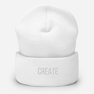 Puede incluir: Gorro de punto blanco con vuelta y la palabra "CREATE" bordada en blanco en la parte delantera.