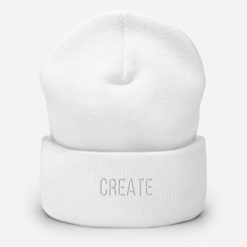 Puede incluir: Gorro de punto blanco con vuelta y la palabra "CREATE" bordada en blanco en la parte delantera.